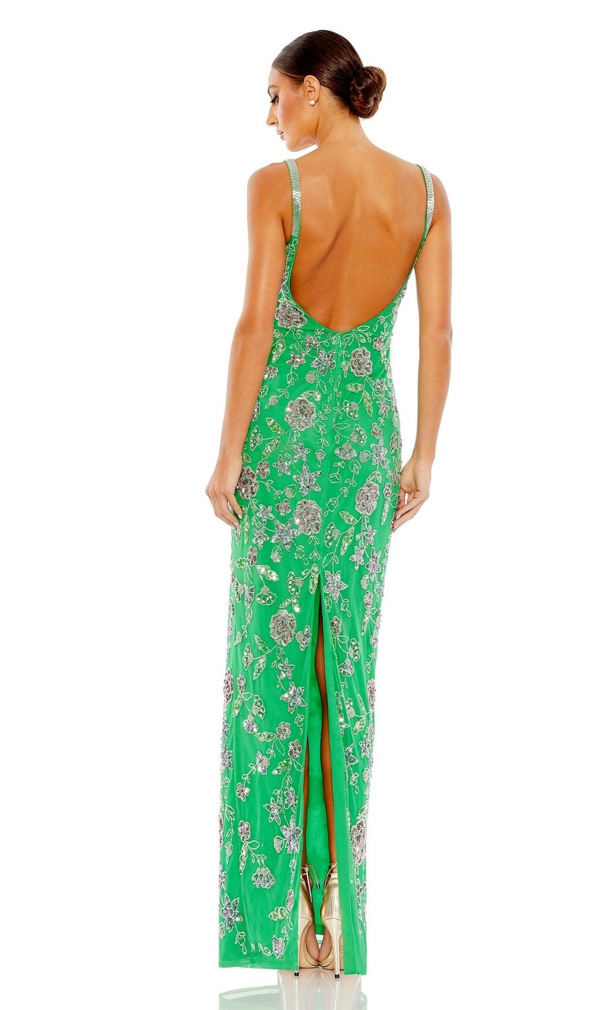 A woman stands with her back to the camera in a green, sleeveless Long Formal Dress 10808 by Mac Duggal, featuring a floral pattern, low back, and slit.