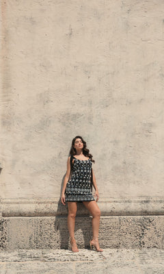 A woman in the Short Wedding Guest Dress 10937 by Mac Duggal stands against a textured beige wall, eyes closed and hands by her sides, exuding relaxed elegance.