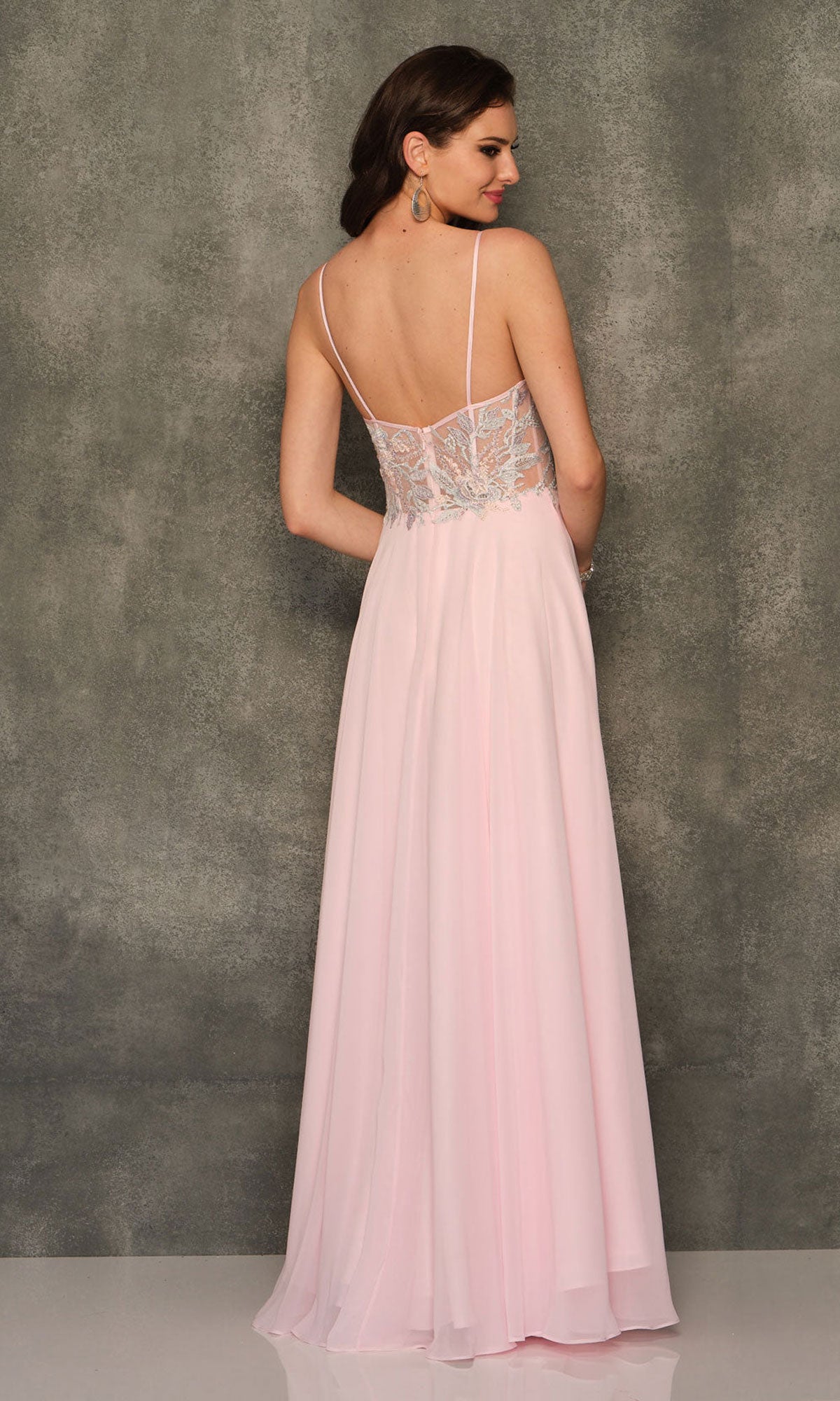 A woman stands before a textured gray wall wearing the Dave and Johnny Long Pink A-Line Prom Dress 10970, which features thin straps and a sheer lace back.