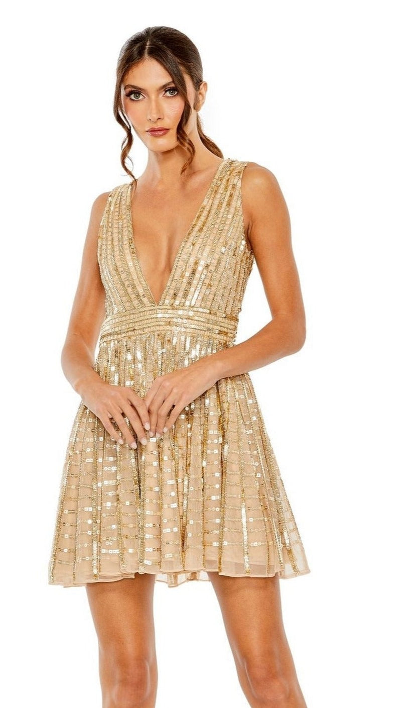 A woman stands against a white background in the Mac Duggal 10982 short gold sequin party dress, featuring a sleeveless deep V-neckline and an A-line skirt.