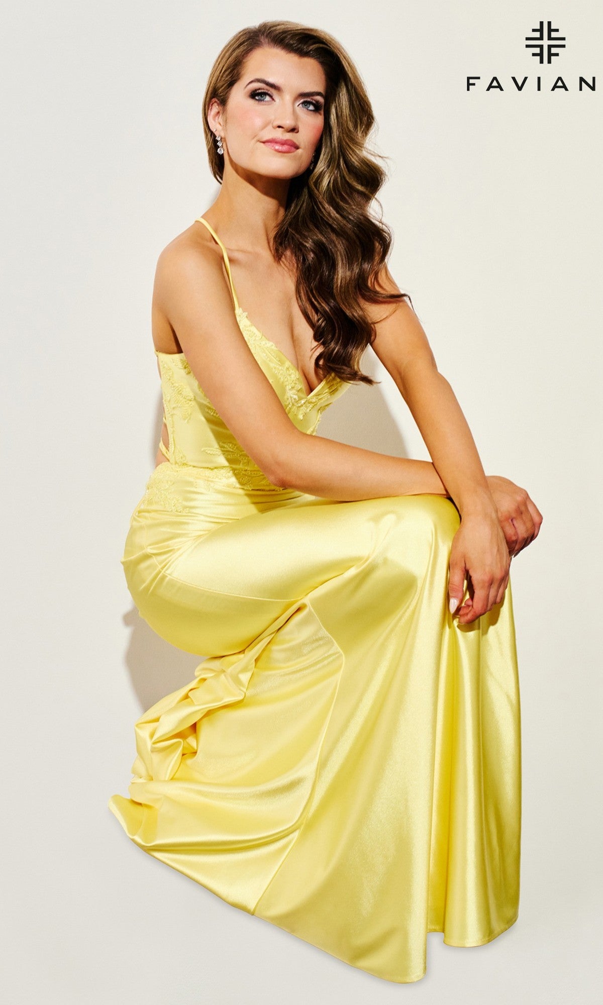 A woman models the Lace-Applique Faviana V-Neck Long Prom Dress 11010, seated against a light background with the Faviana logo in the top right corner.
