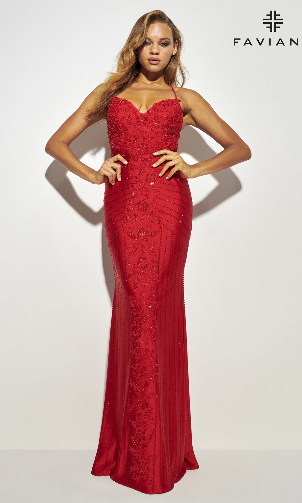 A woman poses against a white background in the Lace-Up Long Faviana Beaded Prom Dress 11021, a fitted red gown with striking beadwork. The 