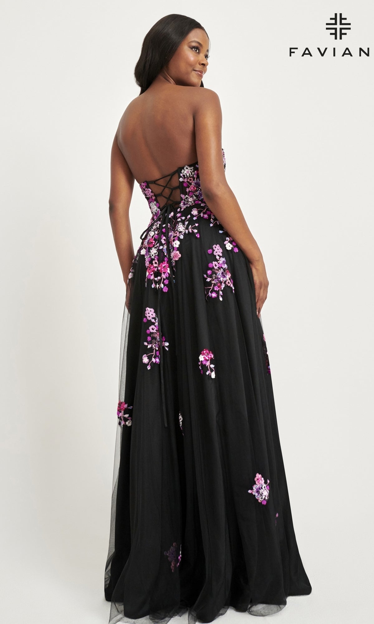 A woman models the Faviana Long Black Strapless Prom Dress 11028, featuring pink and purple floral embroidery, a lace-up back, and a floor-length tulle skirt for an elegant, formal look.