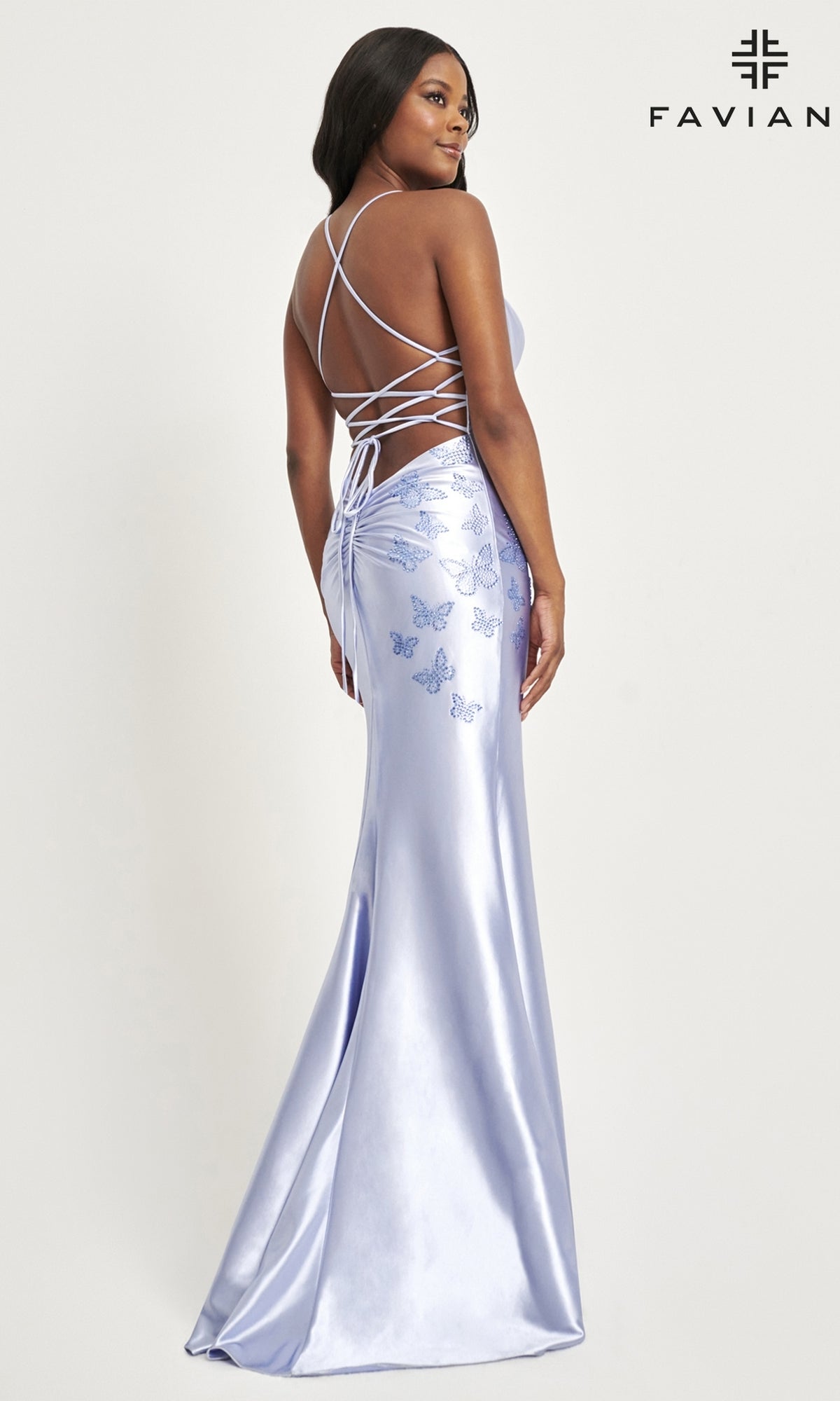 A woman models the Faviana Bead-Butterfly Long Satin Prom Dress 11053 in light purple, showcasing a lace-up open back and beaded butterfly embroidery, standing before a plain background with the Faviana logo in the corner.