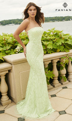 A woman in the Strapless Faviana Long Glitter-Print Prom Dress, featuring a light green hue, stands outdoors by a stone railing with greenery and shimmering water in the background.