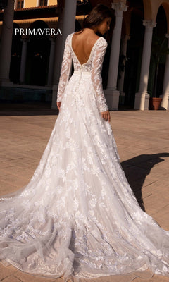 A woman poses outdoors by columns in the Long Wedding Dress 11111 by Primavera, an ivory lace gown with long sleeves and a deep V-back. "PRIMAVERA" appears in the top left corner.
