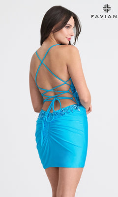 A woman in the Faviana 11116 Strappy-Back Short Homecoming Dress—a bright blue sequin party dress with a low back and crisscross lace-up straps—stands against a plain background with the Favian logo.