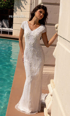 A woman in the Long Wedding Dress 11121 by Primavera—a white, embellished, short-sleeve gown with beaded embroidery and v-neckline—stands poolside against a light wall. "PRIMAVERA" is visible in the background.
