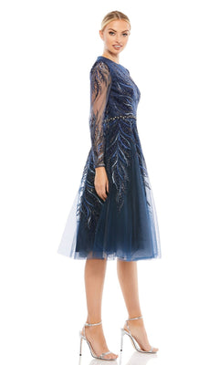 A woman models the Mac Duggal 11136 blue knee-length cocktail dress with sheer long sleeves and silver heels, standing against a plain white background.