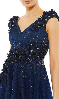 A woman wears the Mac Duggal V-Neck Midnight Blue Formal Dress 11152, an A-line gown with embroidered floral appliques and sparkling embellishments on textured fabric.