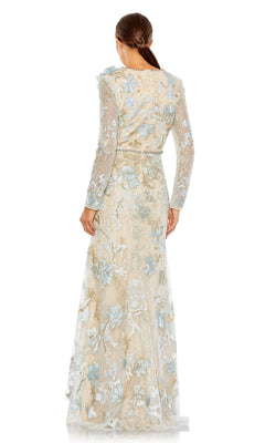 A woman stands facing away, wearing the Long Formal Dress 11174 by Mac Duggal—floor-length, beige with blue floral embroidery, long sleeves, and a fitted waist. Her hair is pulled back in a low ponytail.