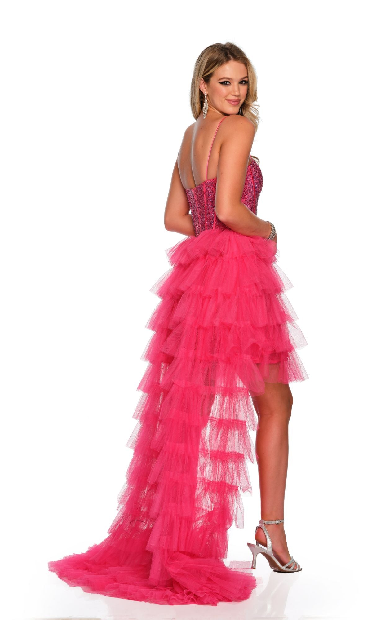 A woman poses in high heels against a white background, wearing the Dave and Johnny Pink High-Low Prom Dress 11174 featuring a fuchsia pink hue, embellished corset bodice, and ruffled skirt.