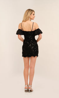 A woman stands with her back to the camera, wearing the Short Sleeve Short Black Homecoming Dress 11181 by Dave and Johnny, paired with silver high heels, set against a neutral background.