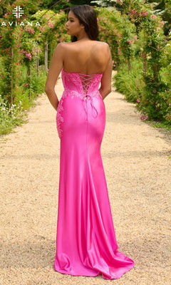 A woman stands on a garden path wearing the Faviana 11209 Strapless Long Corset Prom Dress in bright pink satin with lace-up back and lace detailing, facing away from the camera.