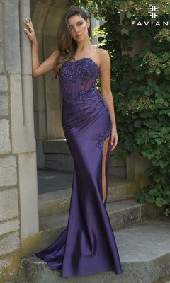 A woman wearing the Strapless Long Corset Prom Dress: Faviana 11209, featuring a satin finish, lace details, and a thigh-high slit, stands against a stone wall and lush greenery.