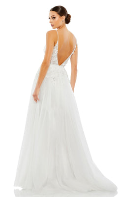 A woman stands facing away in the Long Formal Dress 11228 by Mac Duggal, a white A-line gown with a sheer bodice, v-neckline, deep V-back, lace details, and a long tulle skirt.