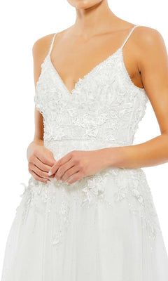 A woman stands with hands clasped, wearing the Long Formal Dress 11228 by Mac Duggal—a white A-line gown featuring thin straps, a V-neckline, and elegant floral lace detailing.