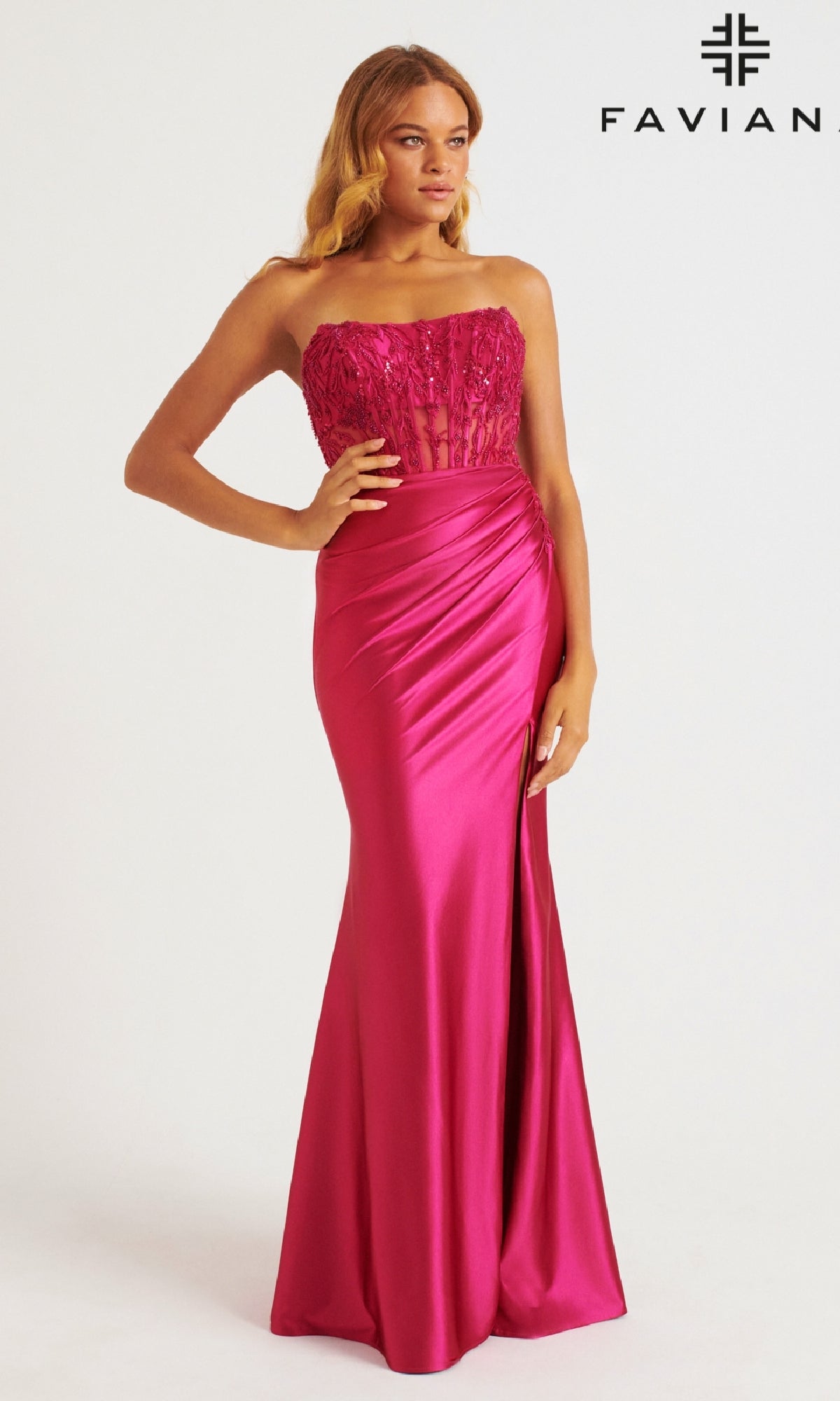 Against a white background, a woman models the Faviana 11246 long prom dress in fuchsia satin. The strapless gown features a corset bodice, sheer accents, and an elegant side slit. 