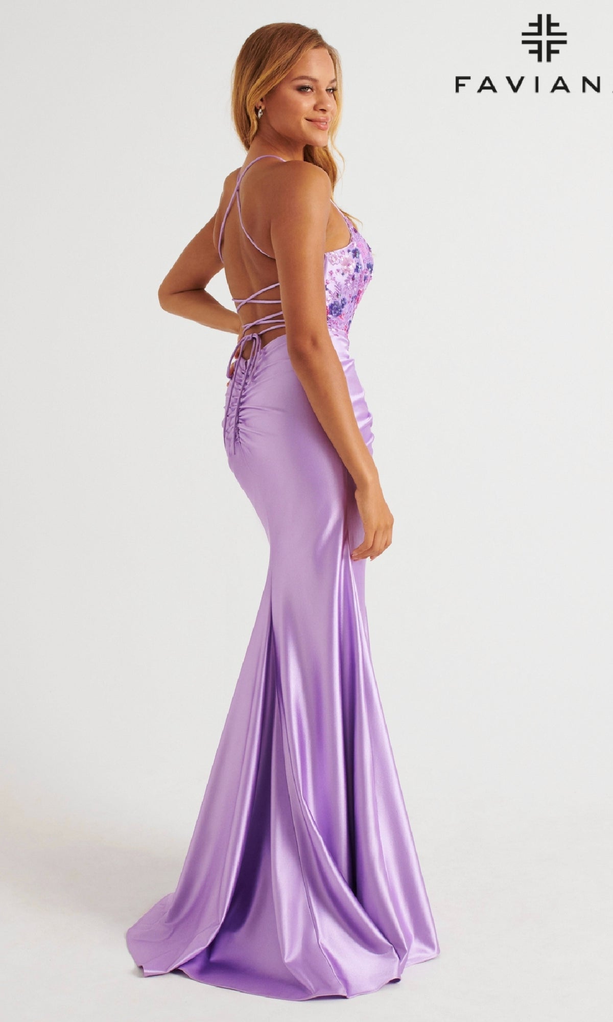 A woman wears the Faviana 11252 long prom dress in lavender, featuring bodycon stretch satin, floral beaded applique, a fitted bodice, and an adjustable lace-up open back. The 