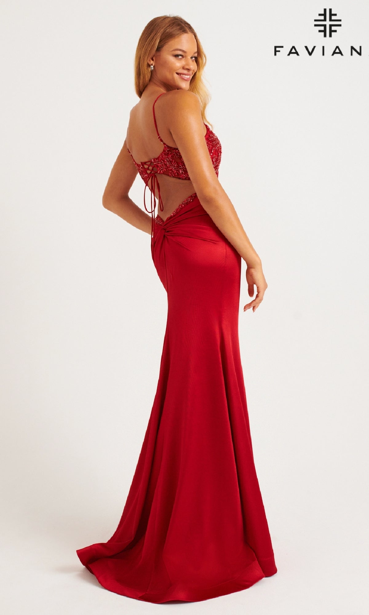 A woman poses and smiles in the Faviana 11256 long red satin prom dress with lace accents and a leg slit. The Faviana logo is displayed in the top right corner.