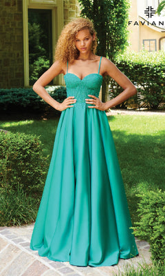 A woman poses outdoors, hands on hips, in front of greenery and a stone building while wearing the Faviana 11259 Lace-Up Long A-Line Prom Dress featuring a teal embroidered-lace corset bodice with spaghetti straps.