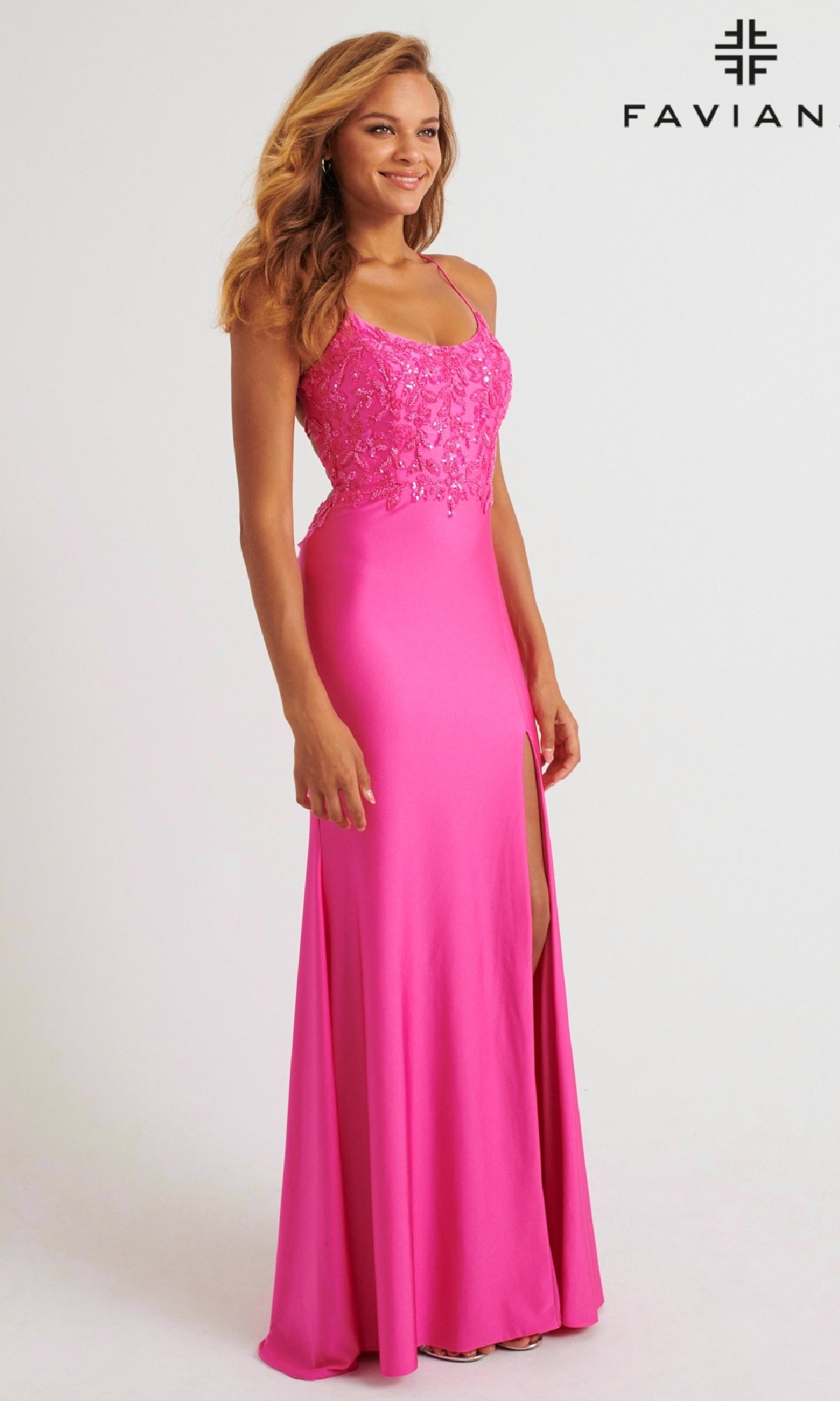 A woman models the Faviana 11264 long prom dress, featuring bright pink charmeuse fabric, a lace bodice, and a thigh-high slit. She stands against a plain background with the 