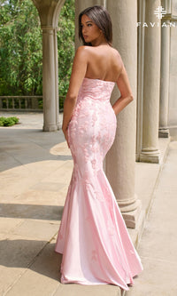 A woman stands outdoors on a stone terrace, wearing the Faviana 11271 long prom dress in light pink, which features a strapless mermaid silhouette, floral embroidery, and a flared hem.