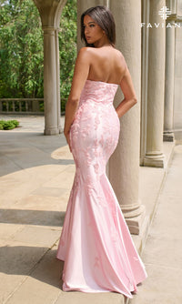 A woman stands outdoors on a stone terrace, wearing the Faviana 11271 long prom dress in light pink, which features a strapless mermaid silhouette, floral embroidery, and a flared hem.
