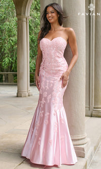 A woman poses outdoors near stone columns and greenery wearing the Faviana 11271 long prom dress, a strapless mermaid gown in light pink with embroidered details.