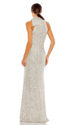 A woman stands facing away in the Mac Duggal 11280 Bow Long Sequin Formal Dress, featuring a large bow detail on one shoulder, sparkling sequins, and her hair tied back for an elegant look.