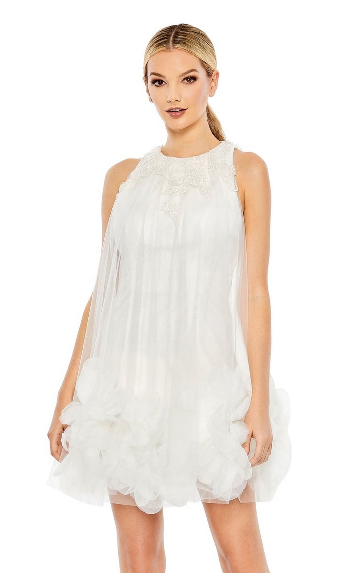A woman wears the Short Homecoming Dress 11294 by Mac Duggal—a sleeveless, short white A-line dress featuring a sheer overlay, lace beaded embellishment, and ruffle hem—standing against a plain background.