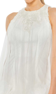 A woman wears the Short Homecoming Dress 11294 by Mac Duggal, a sleeveless white gown with lace beaded neckline embellishments and a sheer fabric overlay.