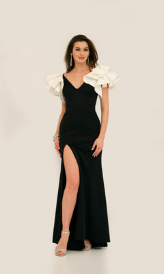 Woman wearing the Ruffle-Shoulder Prom Dress: Dave & Johnny 11314, a striking black evening gown with a thigh-high slit, v-neckline, and large white ruffled shoulder accents, standing against a light background.