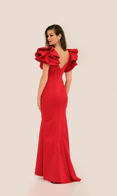 Model in the Ruffle-Shoulder Prom Dress: Dave & Johnny 11314, a floor-length fitted red v-neck gown with dramatic ruffled sleeves, poses looking over her shoulder against a plain light background.