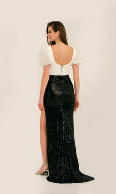 A woman showcases the Long Formal Dress 11328 by Dave and Johnny, a white puff-sleeve, open-back gown paired with a black sequined skirt—an elegant evening look as she stands turned from the camera.