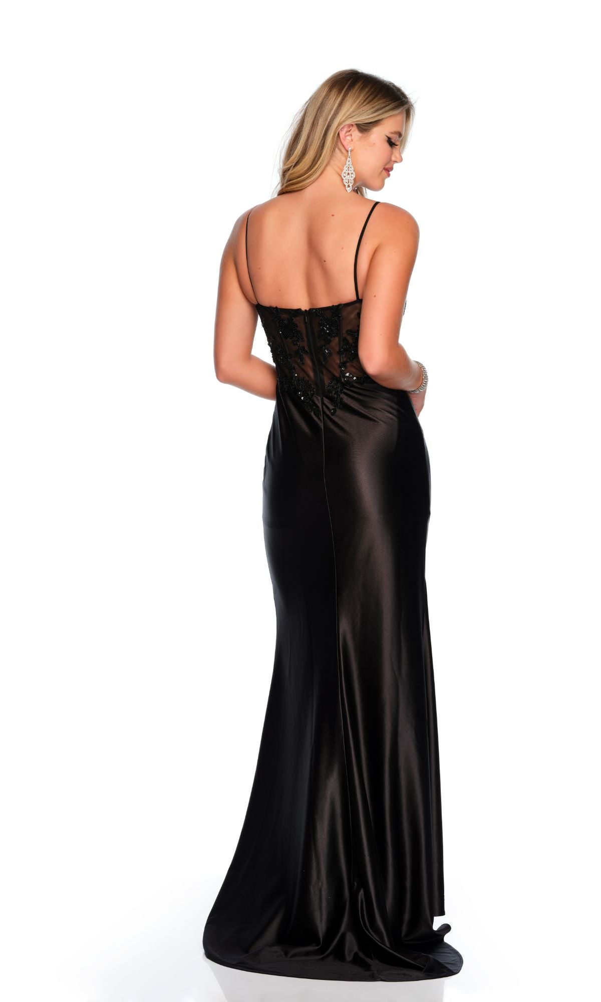 A woman faces away in a Sheer-Bodice Long Prom Dress by Dave & Johnny 11330, highlighting the back of her sleek black satin gown with thin straps and lace detailing.