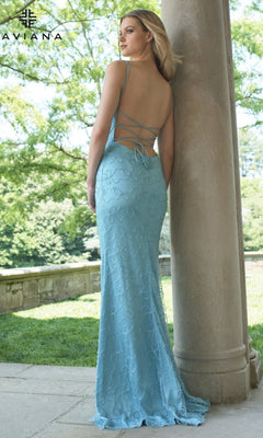 A woman stands outdoors next to a stone column wearing the Faviana 11417 long prom dress in light blue, featuring a v-neckline, thin straps, and a lace-up back. Trees and a stone wall are visible in the background.
