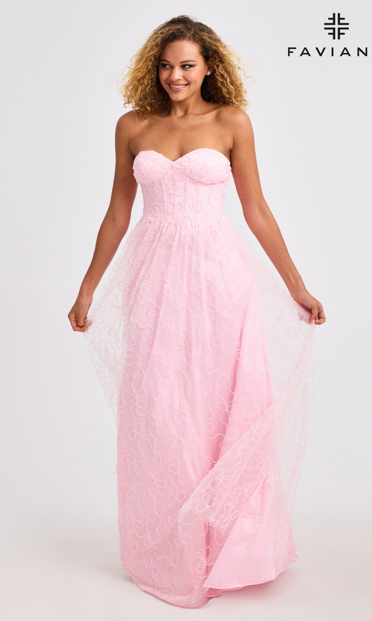 A woman wears the Faviana 11418 Long Prom Dress, featuring a strapless corset bodice and subtle swirl pattern, holding the sides of its floor-length pink skirt. 