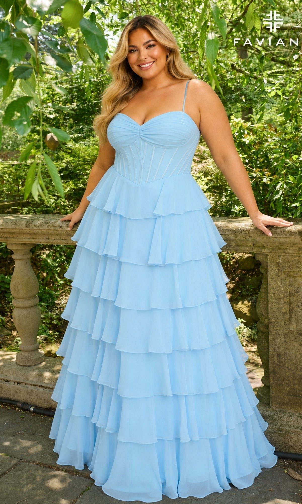 A person wears the sky blue, floor-length chiffon Faviana 11420E Long Plus-Size Prom Dress, featuring a sweetheart neckline and corset-style bodice, while leaning against a stone railing.