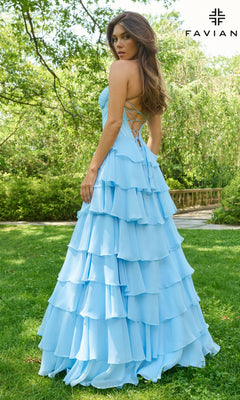 A woman stands outdoors on grass in a light blue Long Prom Dress: Faviana 11420, featuring chiffon fabric, a tiered skirt, backless design, and lace-up corset bodice. Trees are in the background; the Faviana logo appears in the top right corner.
