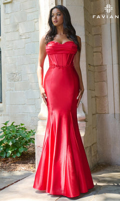 A woman stands outside by a stone wall and greenery, wearing the Faviana 11434— a fitted, strapless mermaid prom dress with a corset bodice.