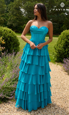 A woman in the Strapless Long Ruffled Prom Gown, Faviana 11436, stands on a gravel path in a garden surrounded by lush shrubs and greenery.