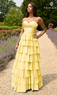 A woman stands on a garden gravel path wearing the Strapless Long Ruffled Prom Gown: Faviana 11436, a yellow tiered dress with a sweetheart neckline. The "FAVIAN" logo is displayed in the upper right corner.