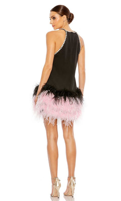 A woman faces away wearing the Mac Duggal Short Homecoming Dress 11437—a sleeveless black dress with pearl accents and a pink and black feathered hem—paired with silver high-heeled sandals.