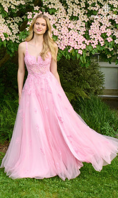 A woman in the Faviana 11437 long prom dress, featuring light pink tulle and delicate lace applique, stands before a blooming tree with pale pink flowers and lush greenery in the background.