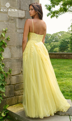 A woman in the Long Prom Dress: Faviana 11438, a yellow sleeveless gown with lace embroidery and a floor-length silhouette, stands outdoors near a stone wall, facing away from the camera.