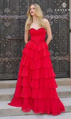 A woman stands before an ornate wooden door, wearing the Faviana 11460 long prom dress with a strapless fitted corset bodice and a flowing tiered ruffle skirt.