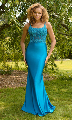 A woman stands outdoors wearing the Faviana 11467, a fitted floor-length turquoise satin prom dress with lace bodice detailing and thin straps, set against a vibrant background of lush greenery and trees.