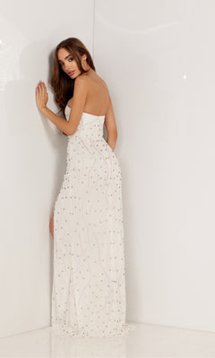 A woman in the Deep V-Neck Strapless Long Beaded Prom Dress 1148, adorned with sequins, stands against a white wall, facing away and looking over her shoulder.