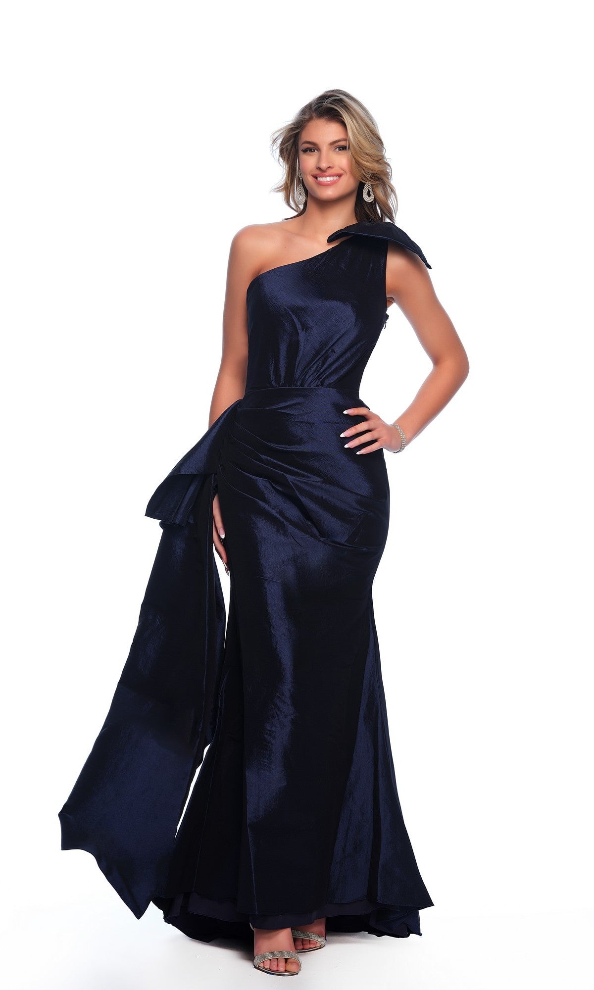 A woman smiles in the Long Formal Dress 11598 by Dave and Johnny, featuring a navy blue, one-shoulder design with a large bow and draped details, as she poses against a plain white background.